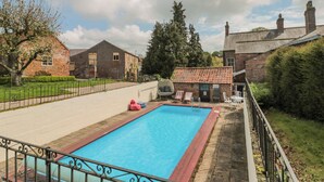 A rectangular swimming pool with a red border, surrounded by a metal fence. There are lounge chairs and a small building with a tiled roof nearby. - Wolds Way (Driffield)