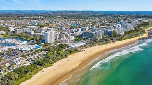 Vue aérienne d’une ville côtière, avec une vaste plage de sable, une zone urbaine densément bâtie et un port de plaisance rempli de bateaux.