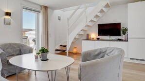 Una sala de estar moderna con una escalera, un televisor de pantalla plana y un comedor con una mesa redonda y sillas.