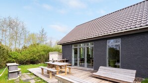 A modern house with a wooden deck, a patio table, and a built-in bench.