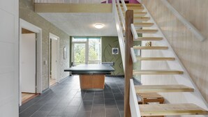 A spacious room with a ping pong table, a staircase, and a view of the outdoors.