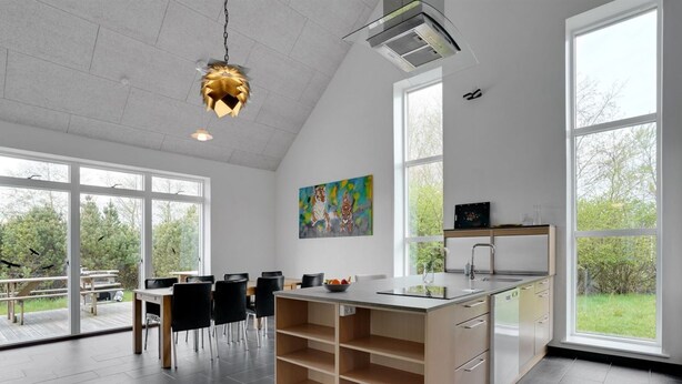 A modern kitchen with a large island, white cabinetry, and a dining area with a view of the outdoors.