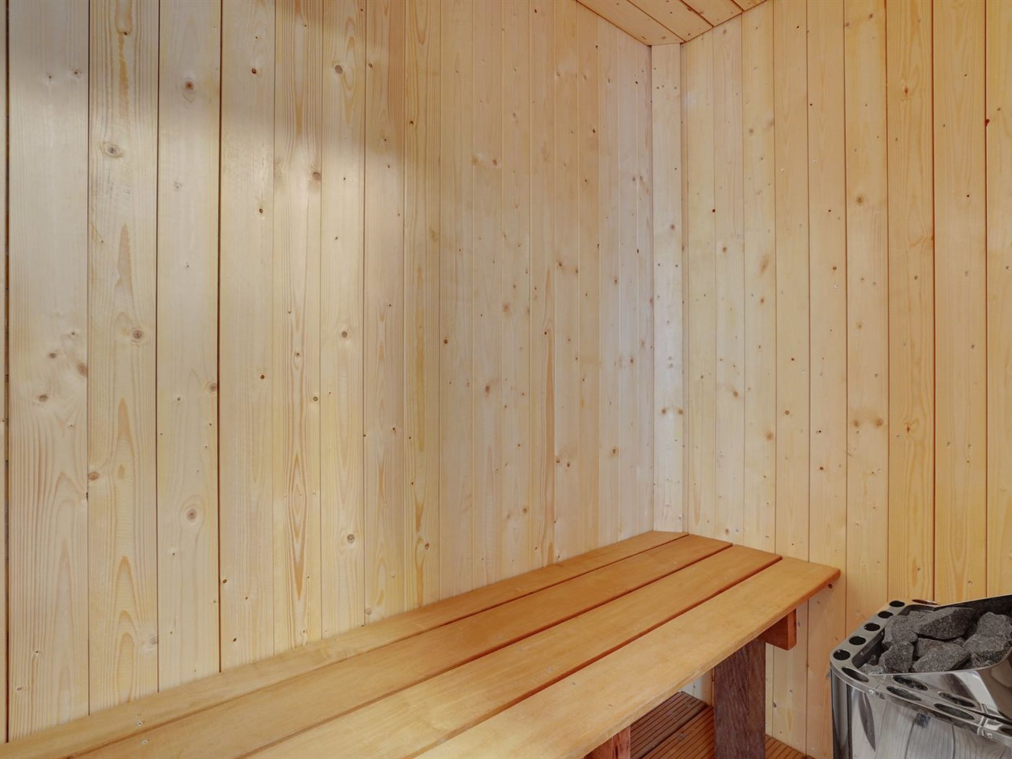 A wooden sauna room with a bench and a sauna heater.
