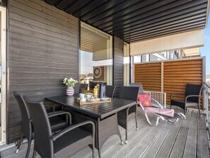 A modern outdoor dining area with a dark wooden table and wicker chairs, a vase of flowers, and a tray with cups and a bottle.