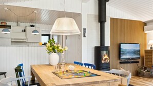 A modern living room with a wooden dining table, blue chairs, a white vase with flowers, a black wood-burning stove, and a TV mounted on the wall. - "Santuzza" - 3.9km from the sea by Interhome (Rømø)