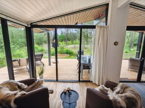 A modern interior with large sliding glass doors leading to an outdoor deck. Inside, there are two leather sofas facing a small round table with candles.