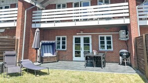 Une maison à deux étages avec un balcon, une terrasse dotée de mobilier d’extérieur et un barbecue.