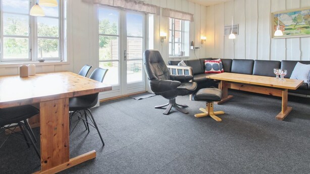 Une pièce avec une table en bois, un fauteuil en cuir noir, un canapé et un tableau accroché au mur.