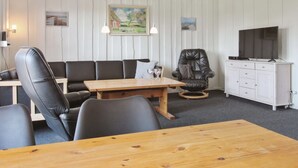 Un salon moderne comprenant un canapé, un fauteuil inclinable, une table basse en bois, un téléviseur et un meuble blanc.