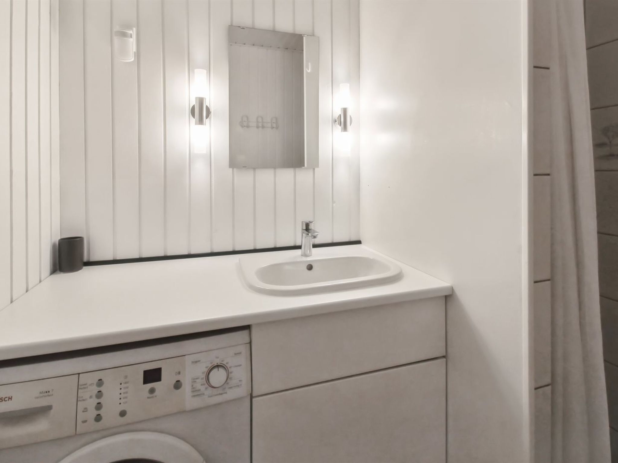 Une salle de bain moderne équipée d’un lave-linge intégré, d’un lavabo et d’un miroir.