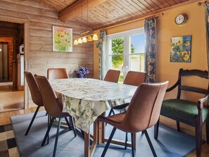 Ein Essbereich mit einem Tisch für sechs Personen, umgeben von Stühlen, in einem Raum mit Holzwänden und einer geneigten Decke.