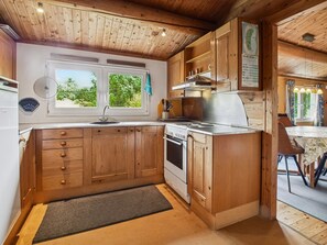 A kitchen with wooden cabinets, a stove, and a window with a view of greenery.