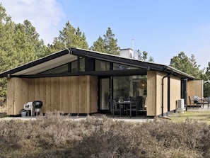A modern house with a large glass door, wooden exterior, and a covered patio area.
