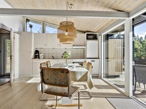 A modern kitchen with a dining area, large windows, and a hanging light fixture.