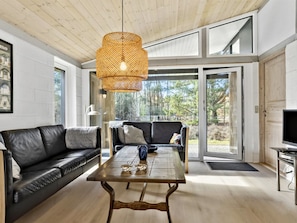 A modern living room with a black leather sofa, a wooden coffee table, and a woven pendant light.