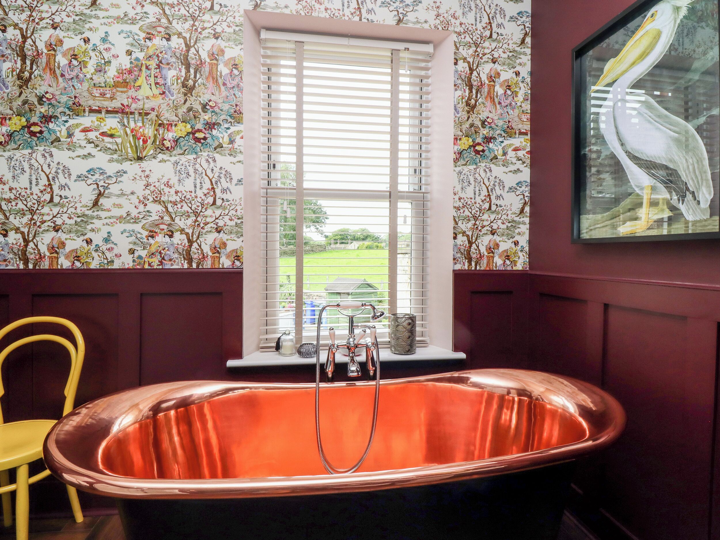 A bathroom with a copper bathtub, floral wallpaper, and a framed painting of a pelican.