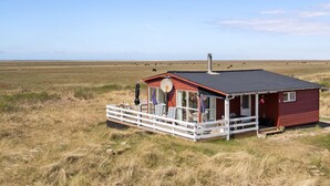 Une cabane rouge avec une véranda, une balustrade blanche et une vue sur le champ ouvert.