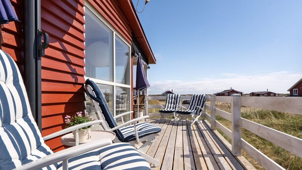 Une terrasse en bois avec des chaises longues à rayures et une table, donnant sur une pelouse avec des maisons en arrière-plan.