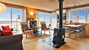 Un salon chaleureux avec une cheminée, des meubles en bois et de grandes fenêtres donnant sur l’extérieur.