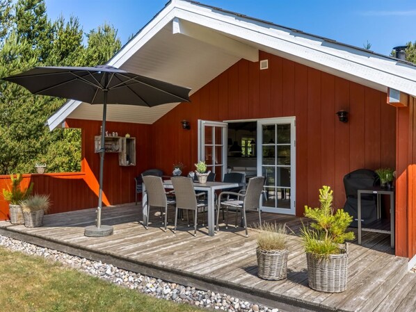 Eine Holzterrasse mit Tisch, Stühlen, einem Grill und Kübelpflanzen.