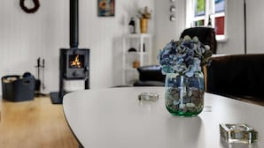 Un salon chaleureux avec une table blanche, un vase rempli de fleurs, une cheminée et une fenêtre donnant sur un beau paysage.