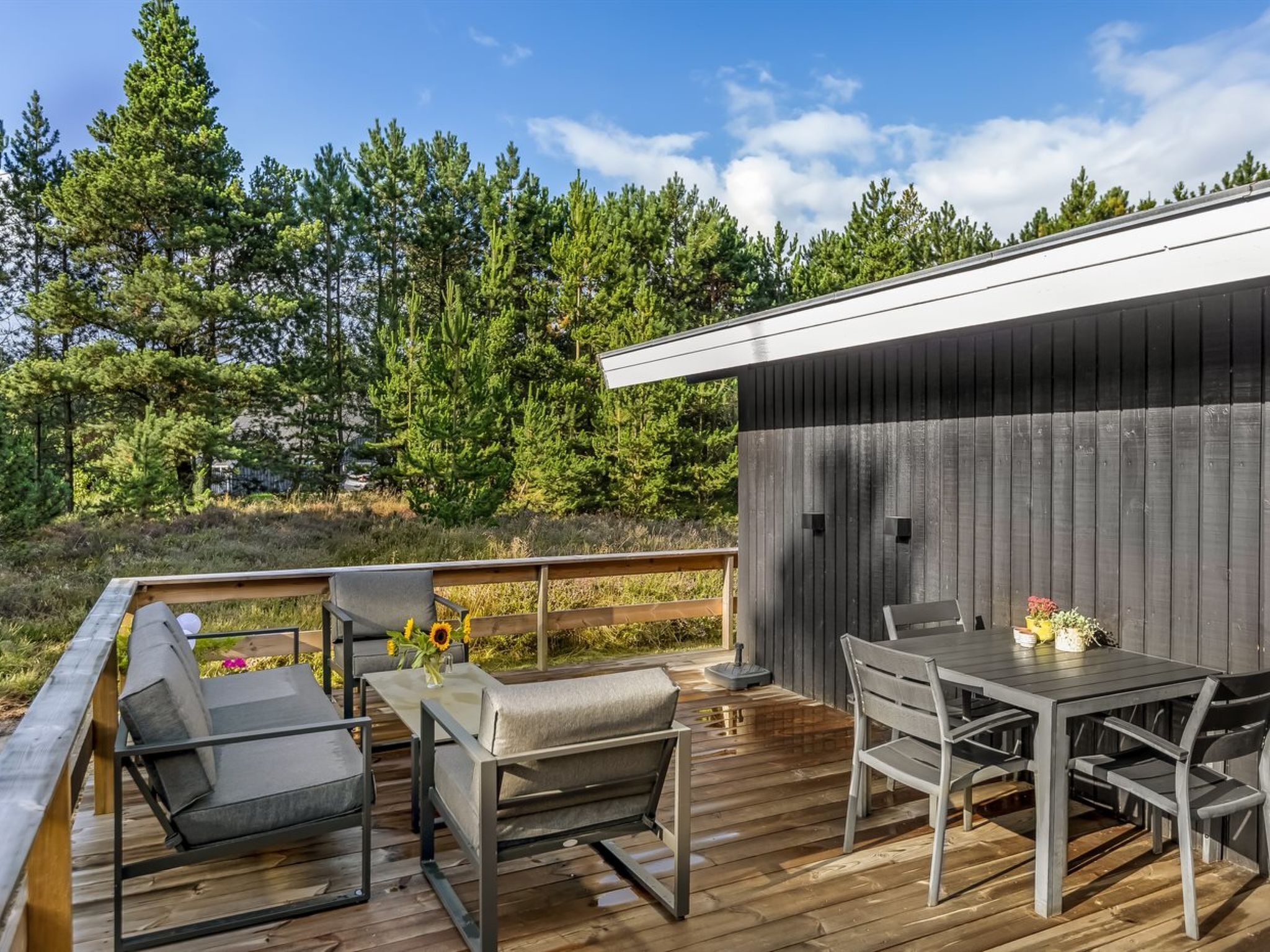A deck with outdoor furniture, a table, and chairs, surrounded by a wooden railing.