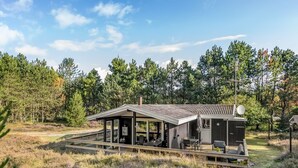 Una cabaña moderna con terraza, rodeada de un bosque denso.