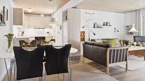 Una cocina moderna con armarios blancos, una zona de comedor con una mesa blanca y sillas negras, y una sala de estar con un sofá y una mesita de centro.