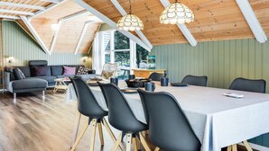 Un loft spacieux avec de hauts plafonds, des poutres apparentes, un coin repas avec une table et des chaises, et un coin salon confortable avec un canapé et des fauteuils.