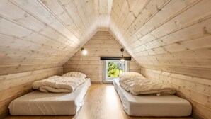 Une petite chambre mansardée avec deux lits simples, un plafond avec des lambris en bois et une fenêtre donnant sur un paysage verdoyant.