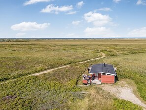 A remote cabin with a single room, a porch, and a small attached shed, surrounded by a vast open field and a clear sky.