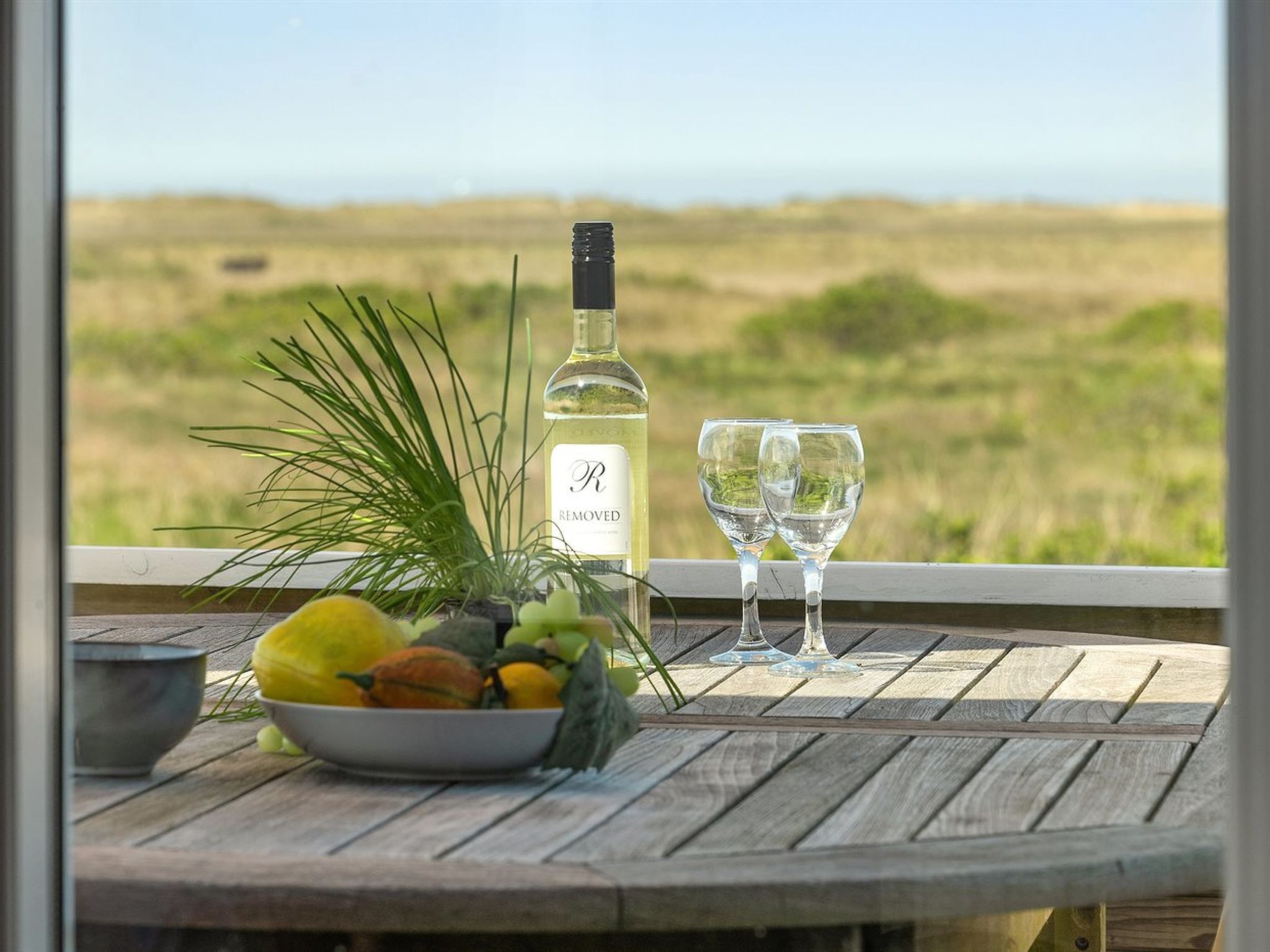 Una mesa con una botella de vino, dos copas y un cuenco de fruta.