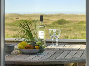 A table with a bottle of wine, two glasses, and a bowl of fruit.