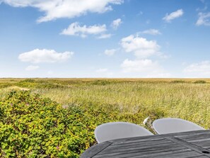 Uitzicht vanuit een houten terras op een grasveld met een heldere lucht.