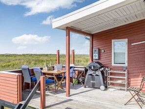 A covered outdoor area with a table and chairs, a grill, and a view of the landscape.