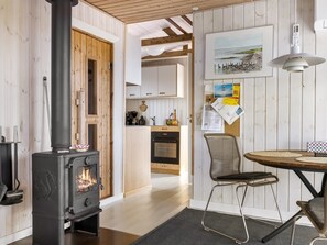 A cozy interior with a wood-burning stove, a dining area with a table and chairs, and a kitchen with cabinets and appliances.