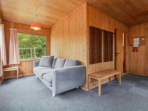 Ein Holzblockbau-Innenraum mit grauem Sofa, einer Bank, einer Holztür und einem Fenster mit Vorhängen.