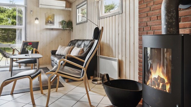 Une pièce chaleureuse avec un canapé en cuir noir, une table à manger avec des chaises, une cheminée et des murs en bois.