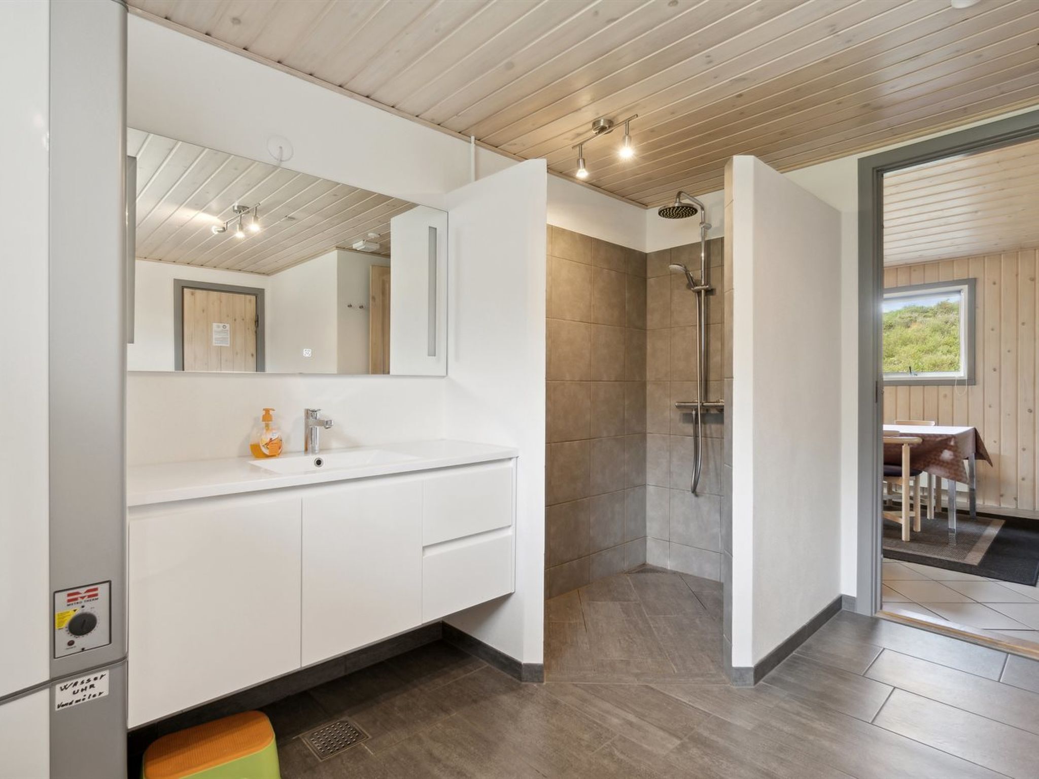 A modern bathroom with a shower, a sink with a mirror, and a view of an outdoor seating area.