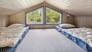 Une chambre avec deux lits, un plafond en pente et une grande fenêtre donnant sur les arbres.