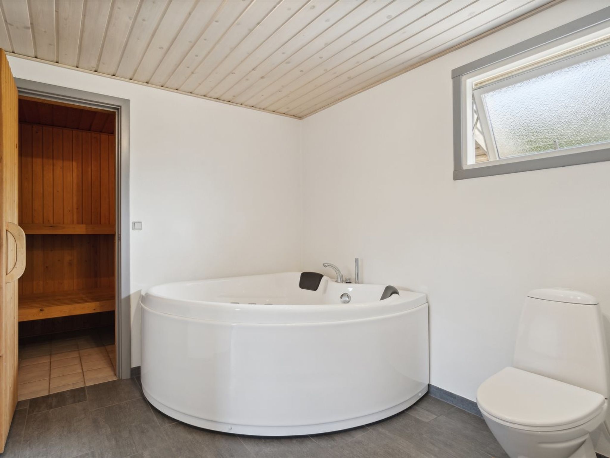 A modern bathroom with a freestanding bathtub, a toilet, and a wooden cabinet.