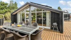 A modern outdoor dining area with a glass-enclosed structure, wicker furniture, and a barbecue grill. - "Lav" - 3.8km from the sea by Interhome (Rømø)