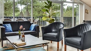 A modern living room with a black leather sofa, two armchairs, and a coffee table. There is a large window with a view of trees and a balcony with outdoor furniture. - "Lav" - 3.8km from the sea by Interhome (Rømø)