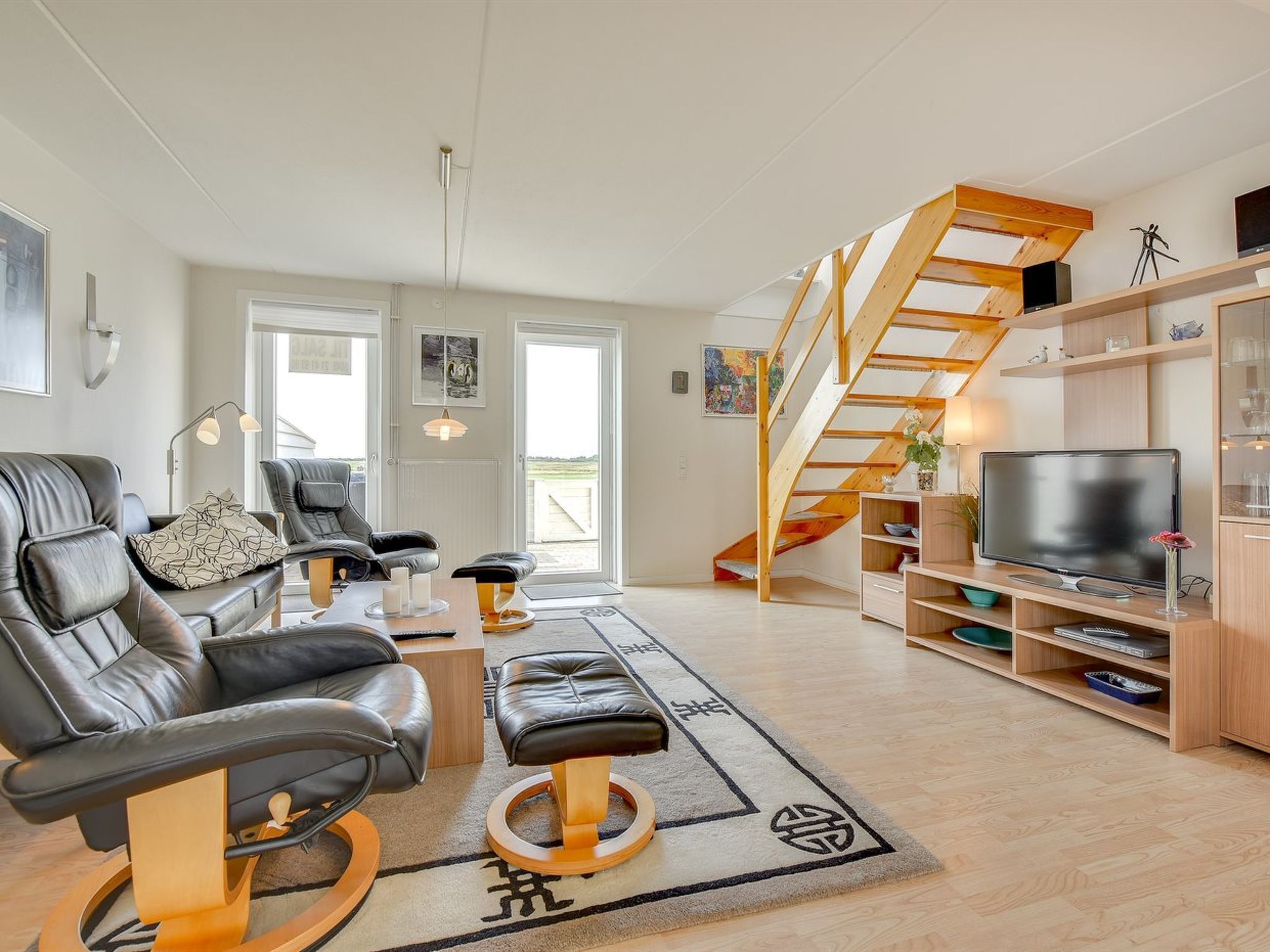 A modern living room with a black leather sofa, a wooden coffee table, and a black leather ottoman. There is a wooden staircase leading to an upper level. - "Helvig" - 2.3km from the sea by Interhome (Rømø)