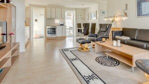 A modern living room with a sofa, a coffee table, and a TV. There is a kitchen in the background with cabinets and a dining area. - "Helvig" - 2.3km from the sea by Interhome (Rømø)