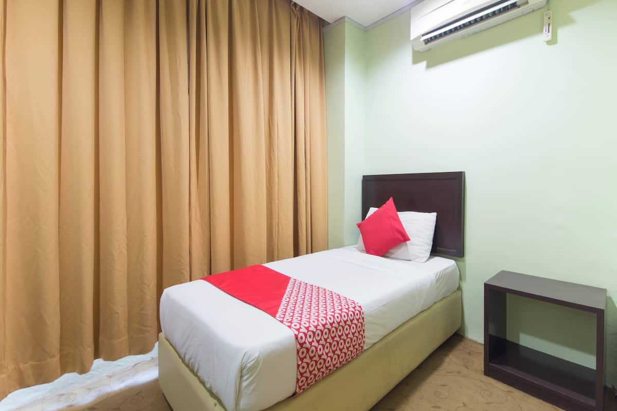 Una cama individual con una colcha estampada, un almohón rojo y una mesita de noche.