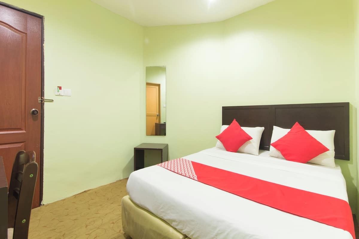 Una habitación de hotel con cama, una puerta de madera, una mesita y un espejo en la pared.