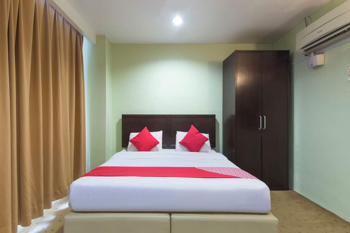 Una cama bien hecha con una colcha blanca y roja, un armario de madera oscura y una mesita de noche color beige en una habitación con paredes verde claro.