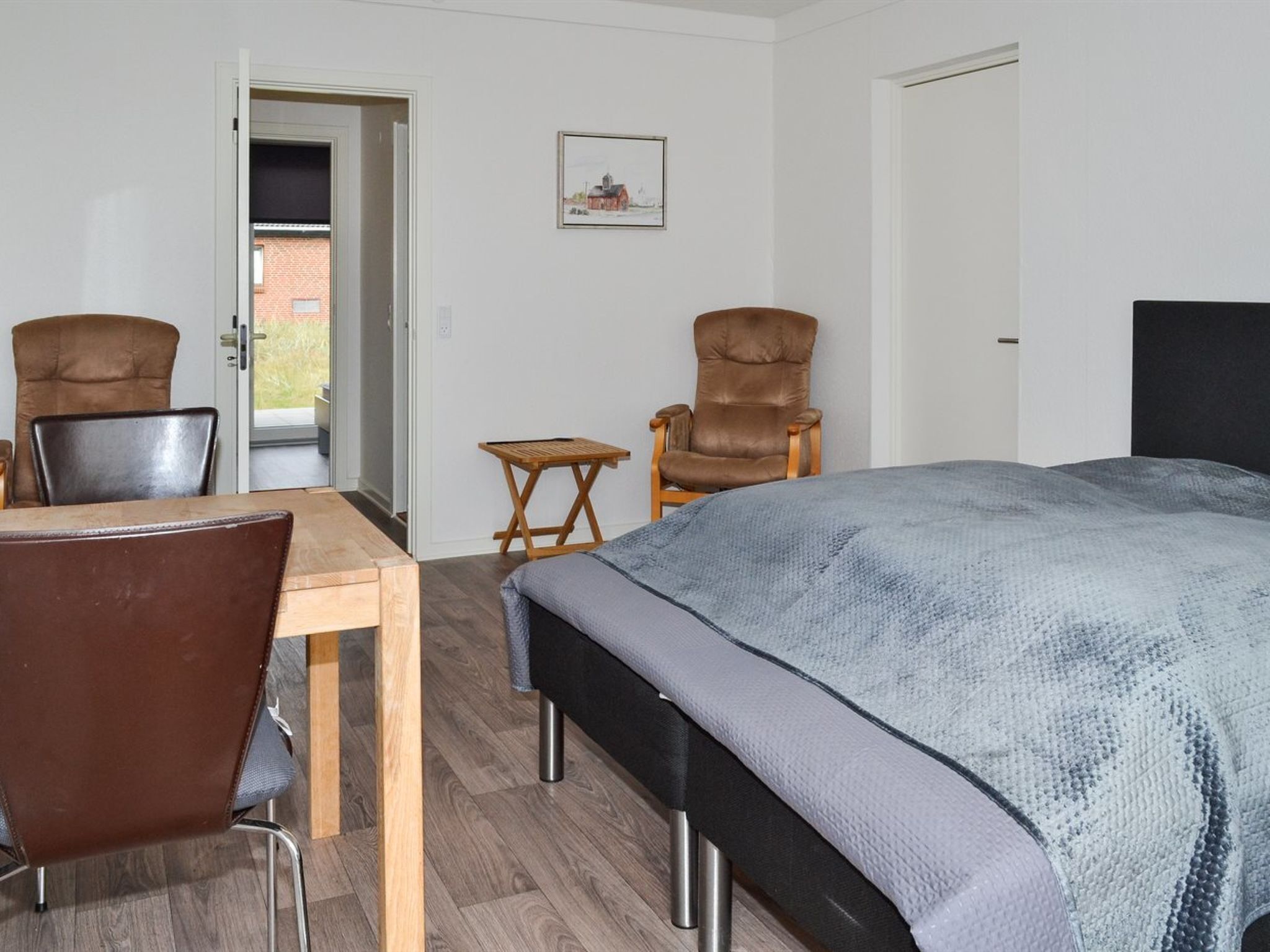 A room with a bed, two chairs, a table, and a small stool.