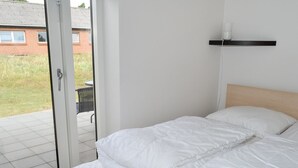 Een slaapkamer met een bed, een schuifdeur die leidt naar een buitenruimte en een kleine tafel met stoelen.